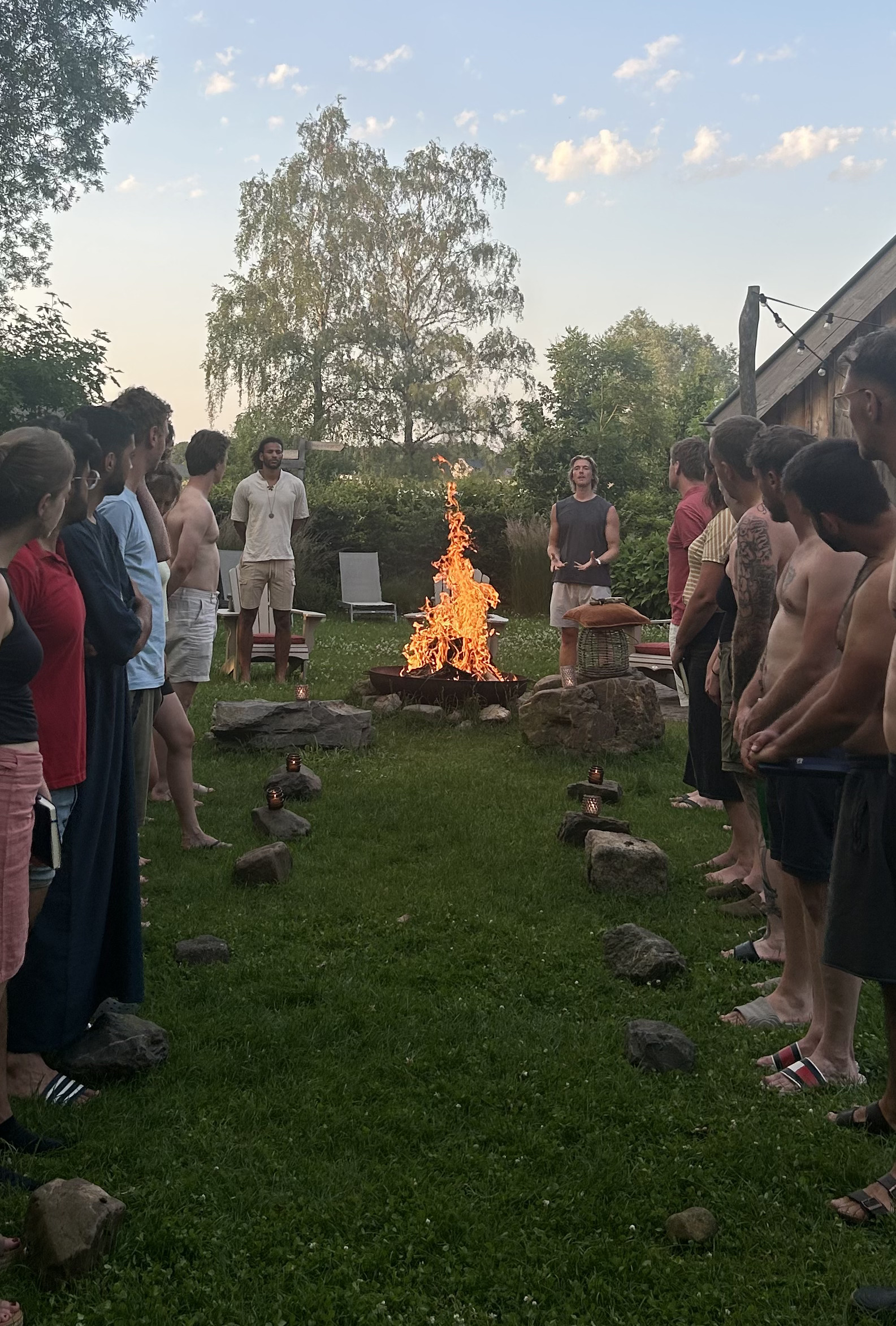 Tommy standing by a fire, holding space for a group gathered in a garden at dusk